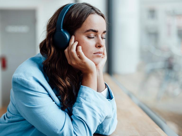 Businesswoman with eyes closed listening music through wireless headphones in office model released property released, G