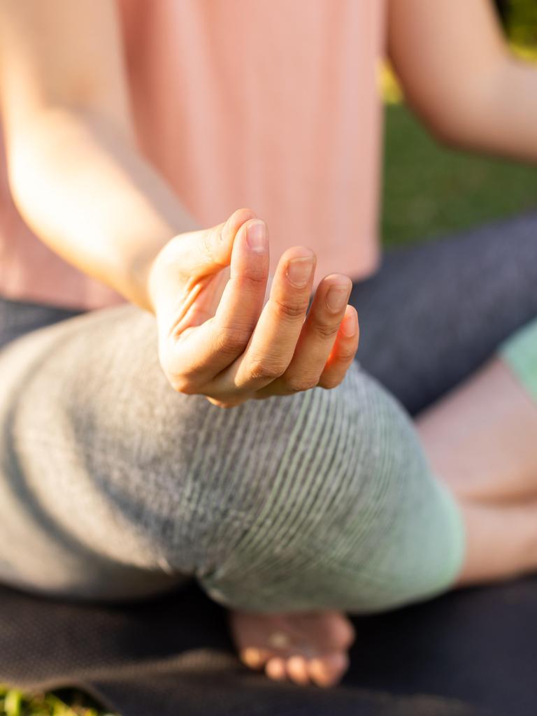 Eine Frau sitzt auf einer Yogamatte und meditiert. Dabei berührt sie mit Zeige- und Mittelfinger die Kuppe des Daumens. 
