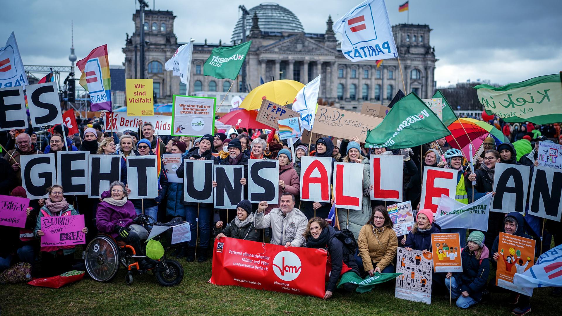 Eine Menschenmenge in Berlin auf der Wiese vor dem Bundestag. Die Menschen schwenken Fahnen und halten große Buchstaben hoch, die sich zu dem Spruch "Es geht uns alle an" formieren.