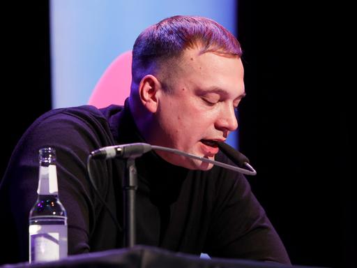Hendrik Bolz sitzt an einem Tisch und liest bei bei der lit.Cologne 2024 Veranstaltung 'Writers Thursday Special' im Theater am Tanzbrunnen. Köln, 14.03.2024
