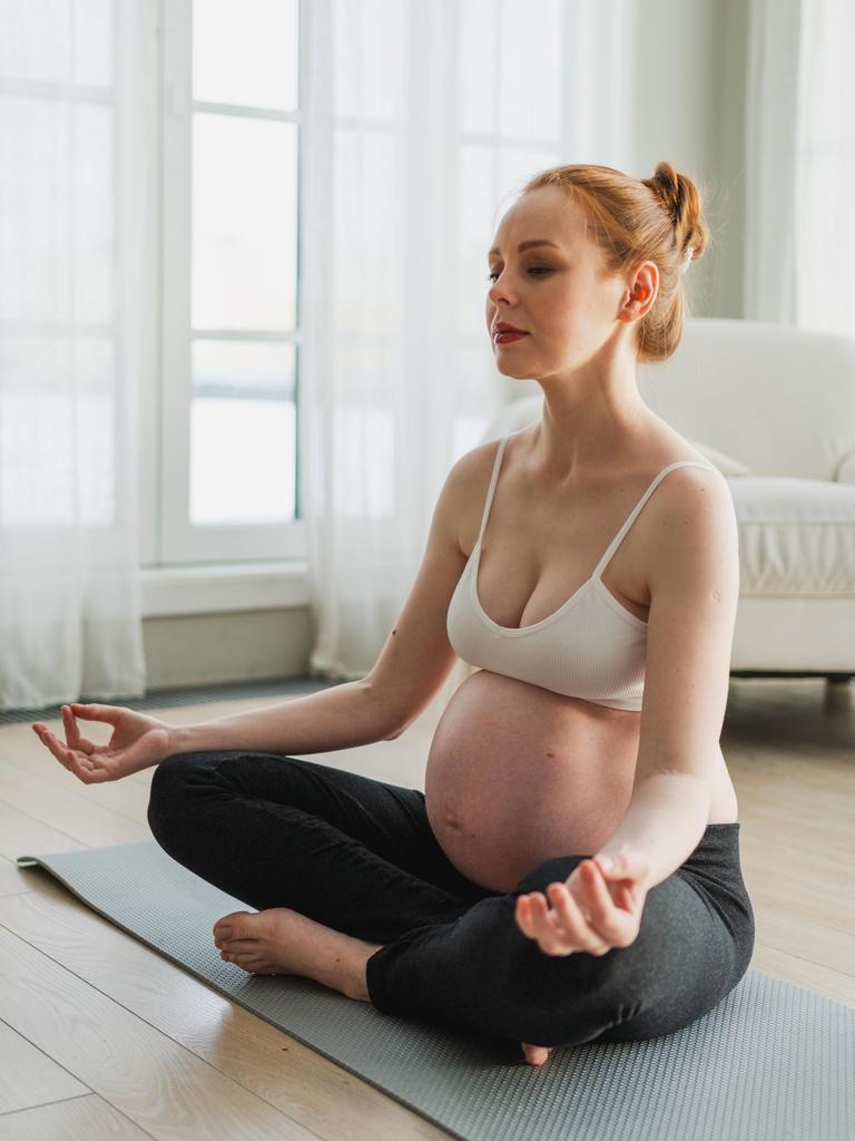 Eine hochschwangere Frau meditiert auf der Yogamatte. Eine hochschwangere Frau meditiert auf der Yogamatte.