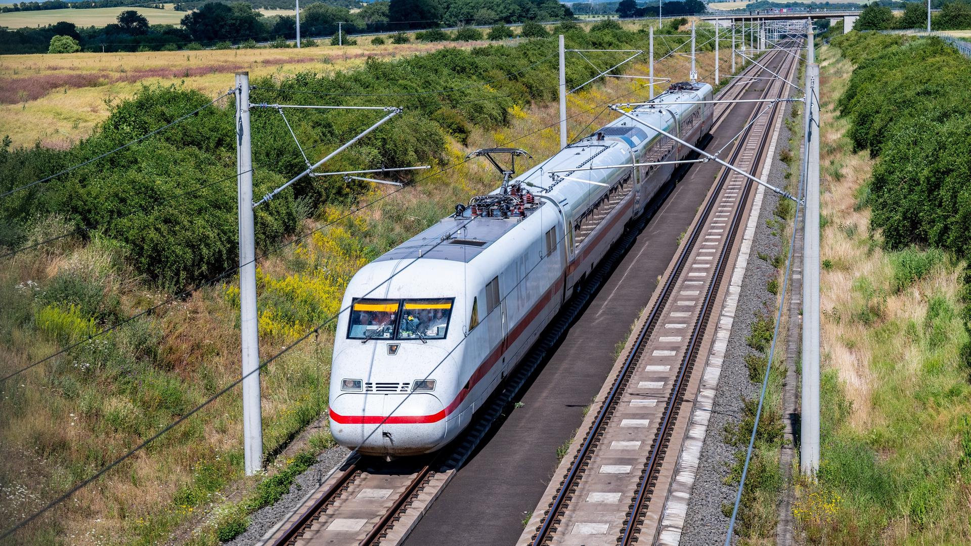Ein weißer Zug mit rotem Streifen und etwas kantigem Vorderteil fährt auf Schienen durch eine Landschaft. Ein weißer Zug mit rotem Streifen und etwas kantigem Vorderteil fährt auf Schienen durch eine Landschaft.