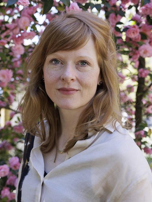 Anja Kampmann steht für ein Porsträt vor einem blühenden Rosenstrauch.