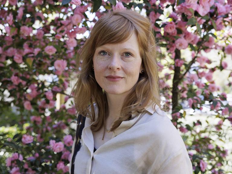 Anja Kampmann steht für ein Porsträt vor einem blühenden Rosenstrauch.