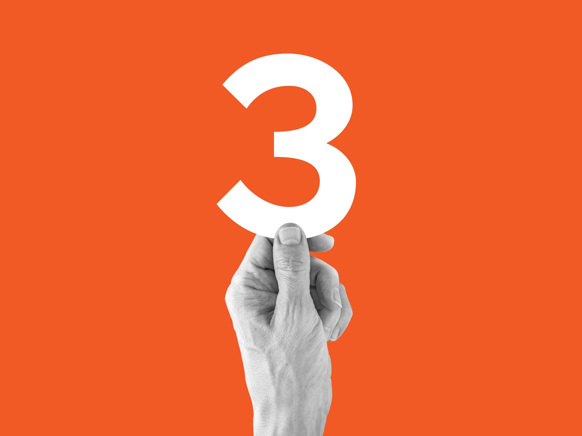 Eine Hand vor orangenem Hintergrund, die eine große 3 hochhält
