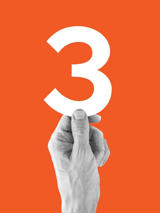 Eine Hand vor orangenem Hintergrund, die eine große 3 hochhält Eine Hand vor orangenem Hintergrund, die eine große 3 hochhält