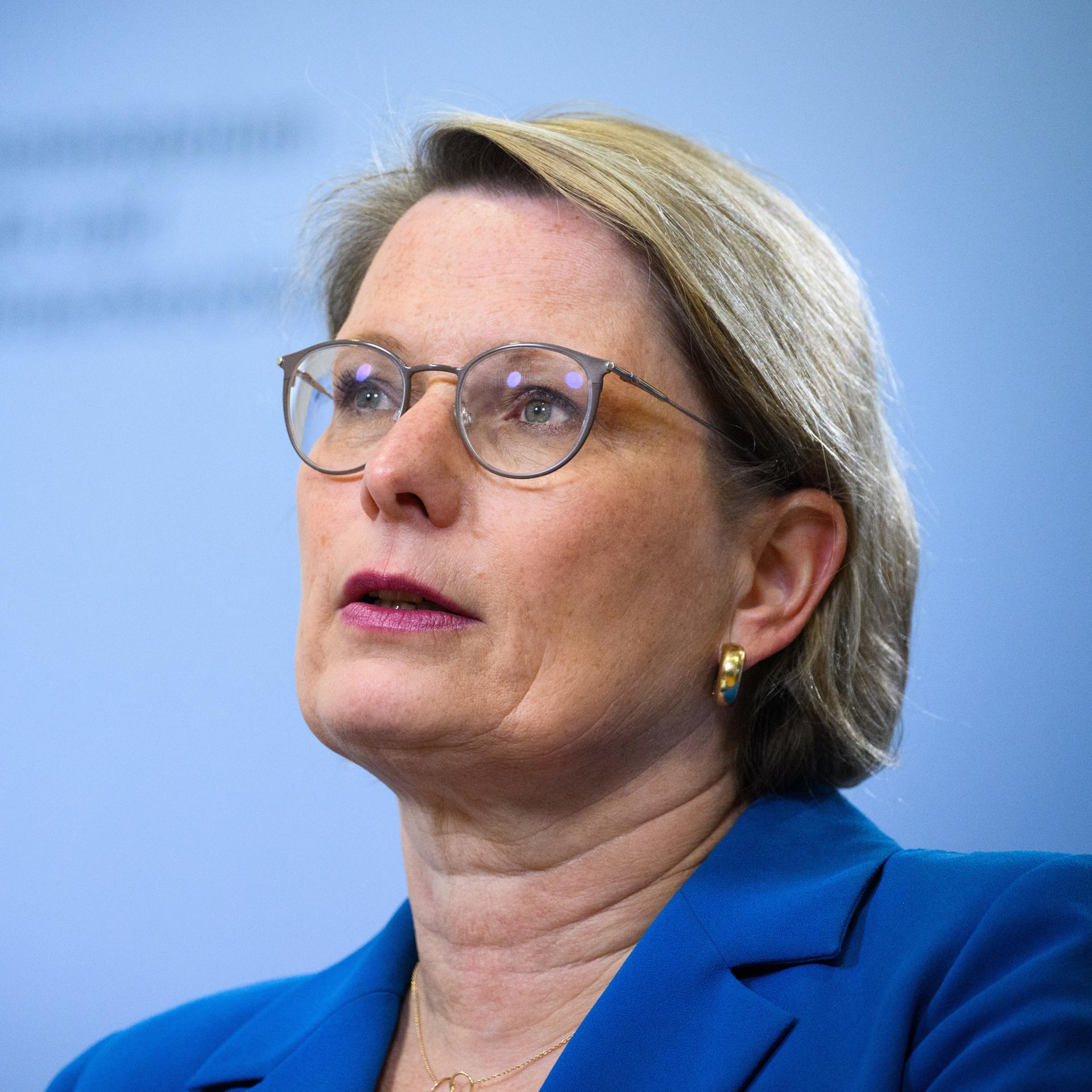 Stefanie Hubig spricht bei einer Pressekonferenz vor einem hellblauen Hintergrund in ein Mikrofon.