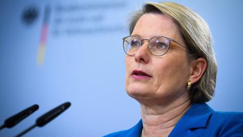 Stefanie Hubig spricht bei einer Pressekonferenz vor einem hellblauen Hintergrund in ein Mikrofon.
