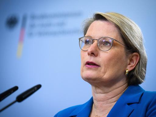 Stefanie Hubig spricht bei einer Pressekonferenz vor einem hellblauen Hintergrund in ein Mikrofon.