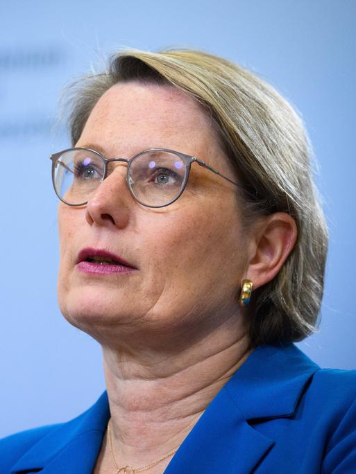 Stefanie Hubig spricht bei einer Pressekonferenz vor einem hellblauen Hintergrund in ein Mikrofon.