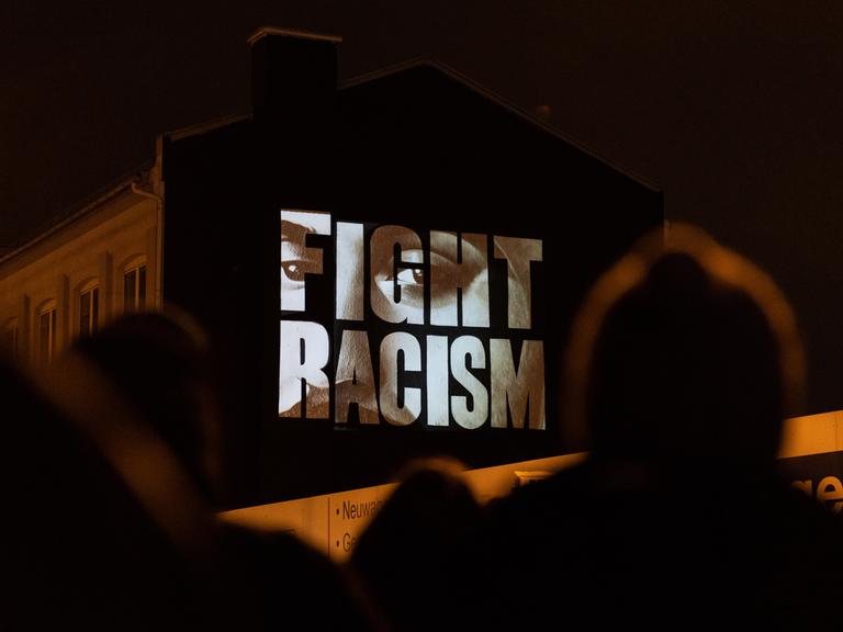 "Fight Racism" mit den Gesichtern der Opfer steht auf einer Hausfassade an der Camberger Brücke zum Gedenken an die Opfer der rassistisch motivierten Anschläge von Hanau im Jahr 2020. Das Künstlerkollektiv "Kollektiv ohne Namen" führte die Aktion durch.
