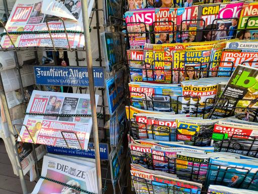 An einem Kiosk sind verschieden Zeitschriften und Zeitungen in Ständern zu sehen