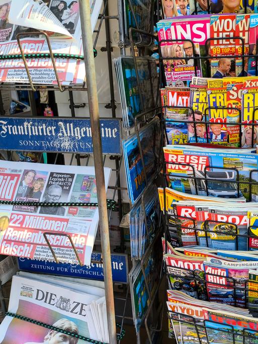 An einem Kiosk sind verschieden Zeitschriften und Zeitungen in Ständern zu sehen An einem Kiosk sind verschieden Zeitschriften und Zeitungen in Ständern zu sehen