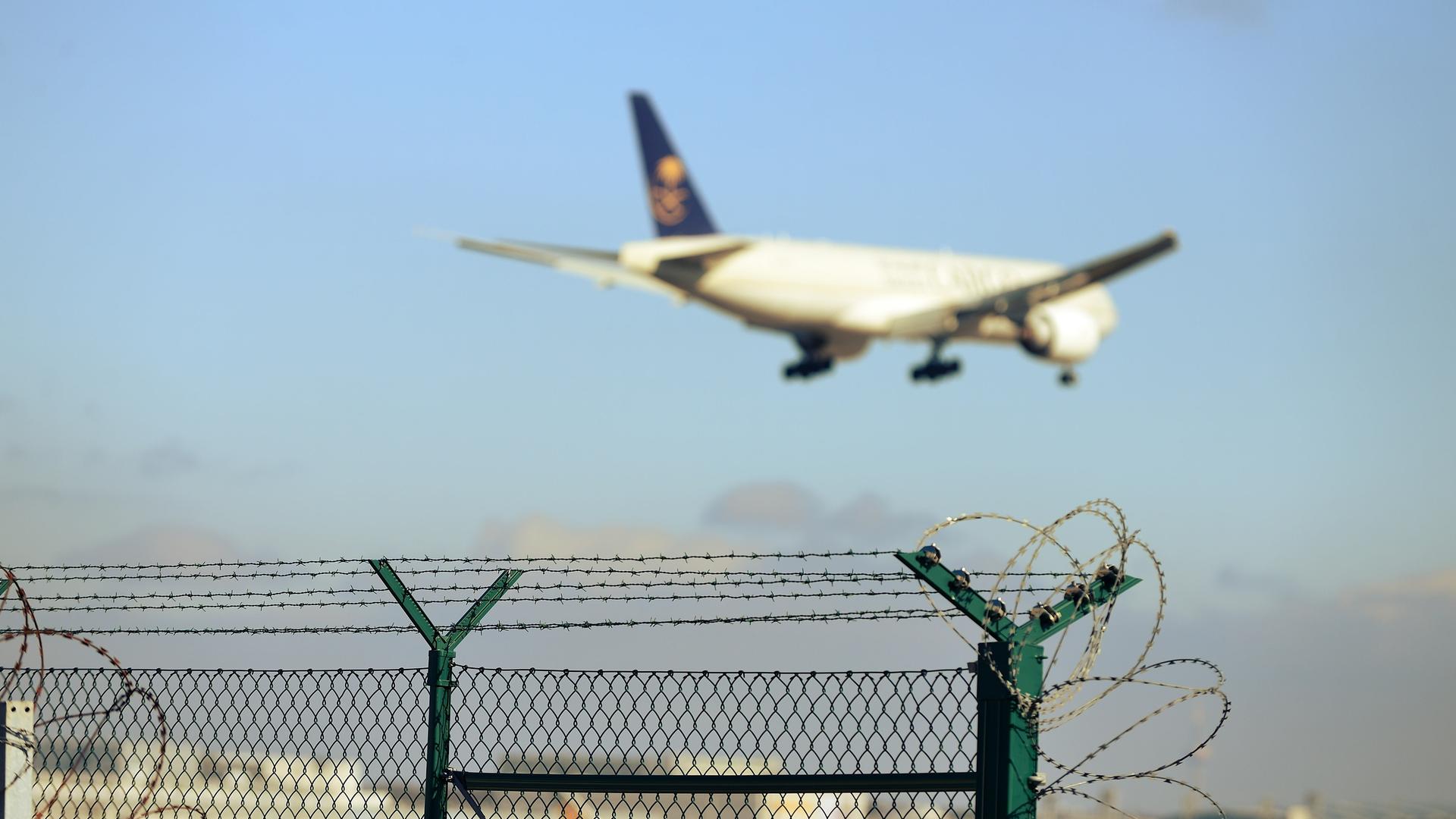 Ein Flugzeug startet, im Vordergrund ist ein Zaun mit Stacheldraht zu sehen