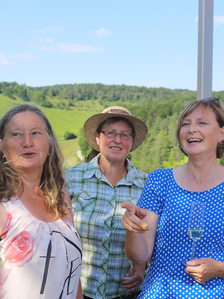 Drei Landfrauen stehen zusammen, im Hintergrund sind Felder und Wald zu erkennen.