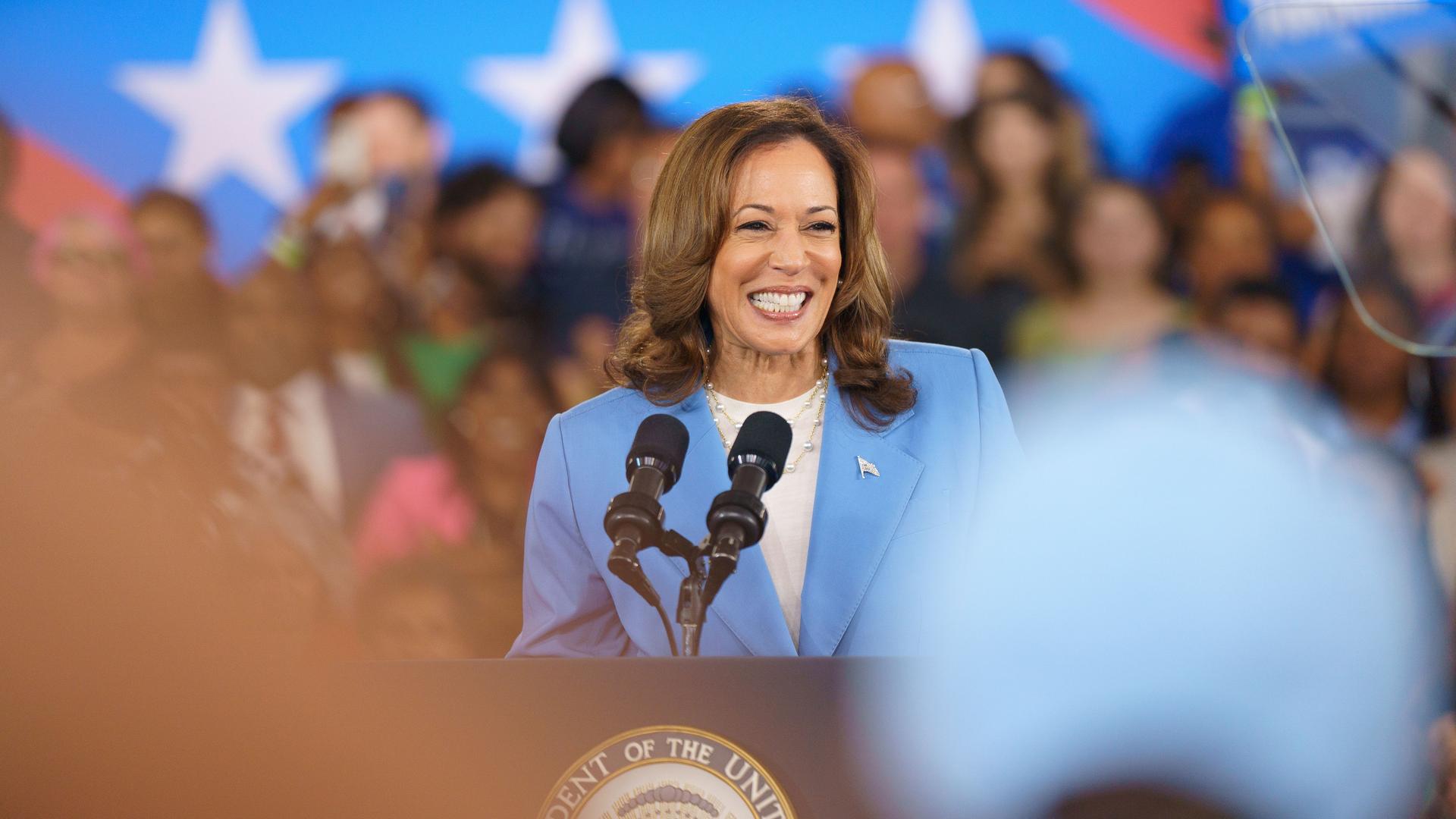 Kamala Harris steht lächelnd auf einem Rednerpult.