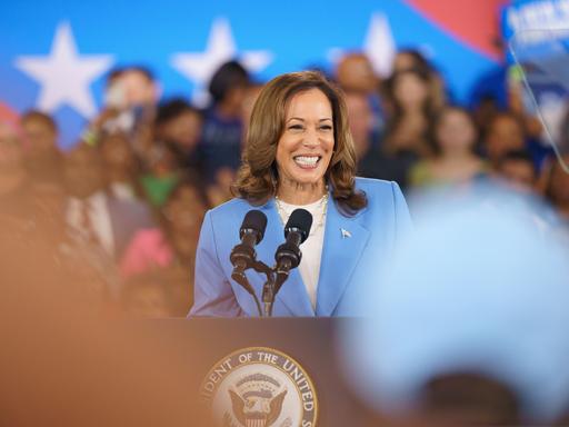 Kamala Harris steht lächelnd auf einem Rednerpult.