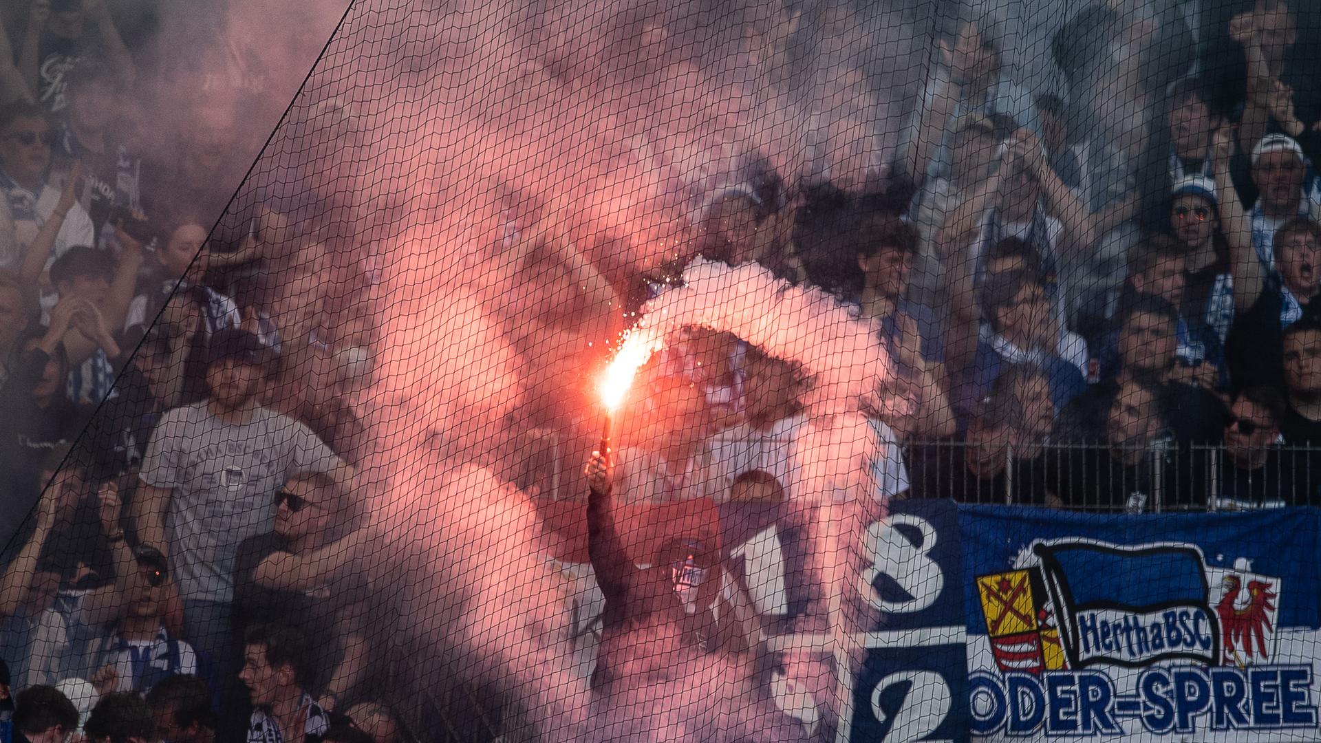 Fußballfans auf der Gästetribüne. Ein Fan hält ein brennendes bengalisches Feuer in der Hand. Die rote Flamme erleuchtet den Block. Starker rauch breitet sich aus.