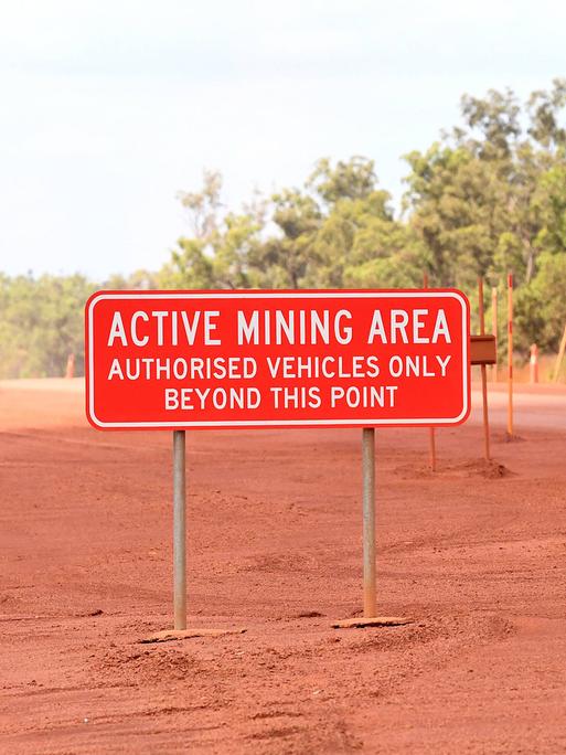 Ein Schild mit der Aufschrift "Active Mining Area - Authorized Vehicles Bexond This Point" vor einer Bauxit-Mine in Australien.