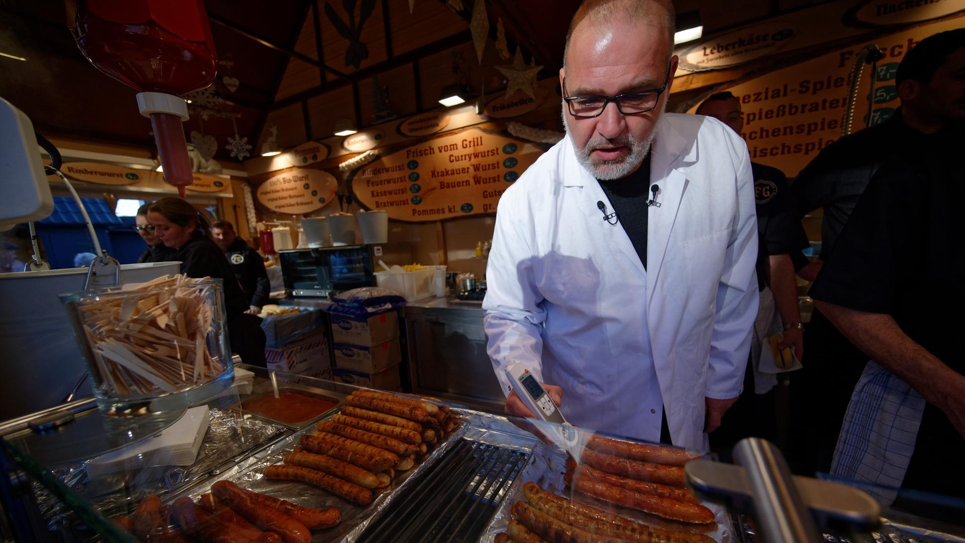 Ein Mann in einem weißen Kittel hält ein Thermometer an Bratgut.