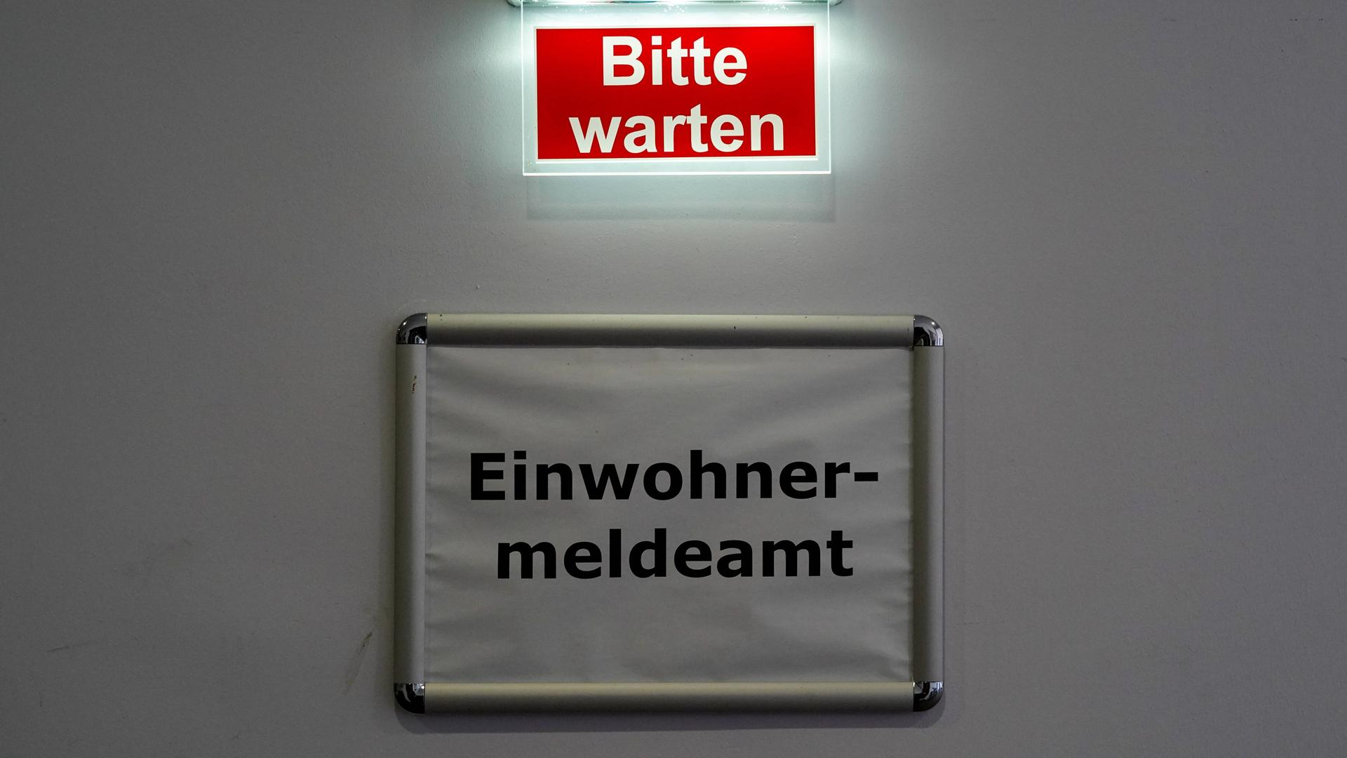 Über dem Schild "Einwohnermeldeamt" leuchtet der Schriftzug "Bitte warten".