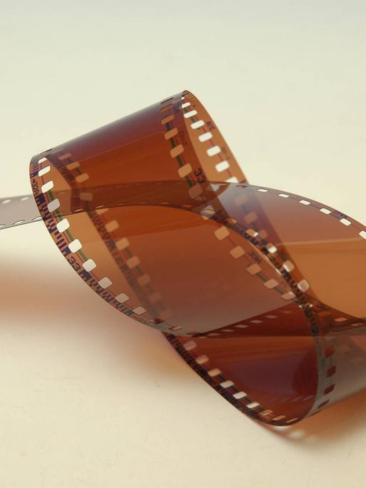Analoger Kleinbild-Filmstreifen verknotet auf gelblichen Untergrund.