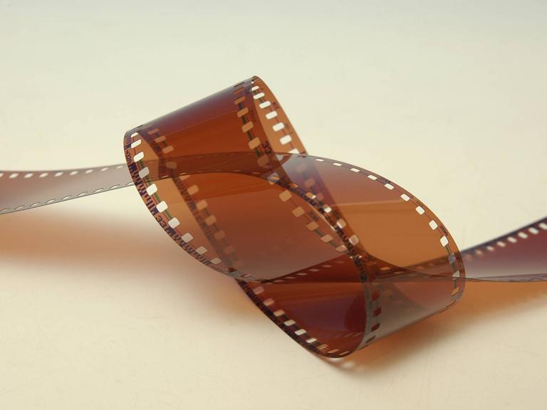 Analoger Kleinbild-Filmstreifen verknotet auf gelblichen Untergrund.