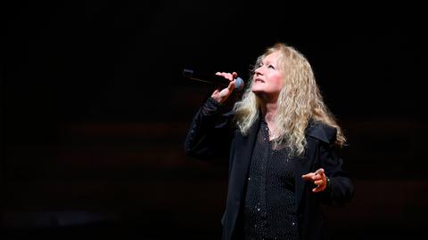 Nicole steht bei ihrer Jubiläumstournee in der Meistersingerhalle Nürnberg mit einem Mikrofon posierend vor schwarzem Hintergrund auf der Bühne.