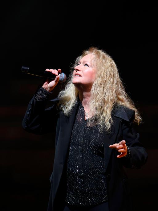 Nicole steht bei ihrer Jubiläumstournee in der Meistersingerhalle Nürnberg mit einem Mikrofon posierend vor schwarzem Hintergrund auf der Bühne.