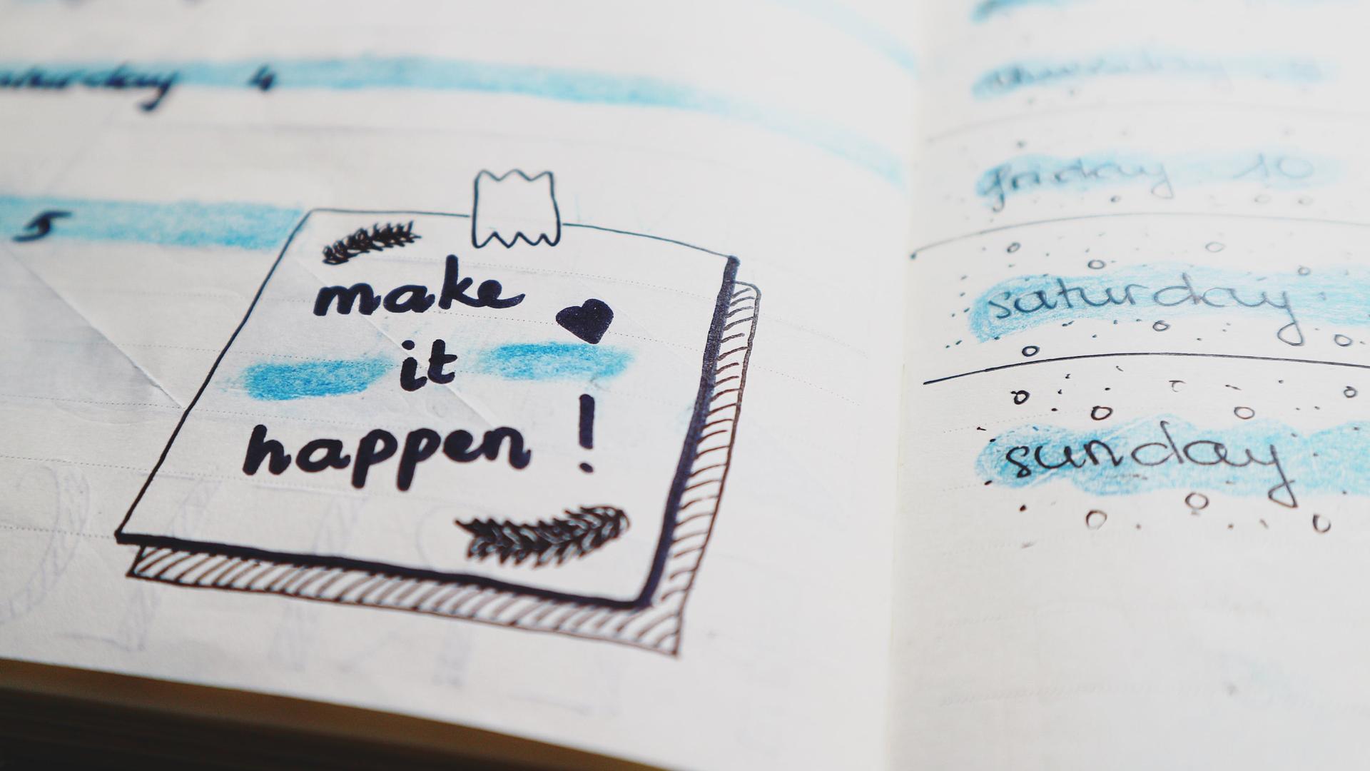 Ein aufgeschlagener Kalender enthält eine kleine Zeichung, die den Schriftzug "Make it happen" trägt. 