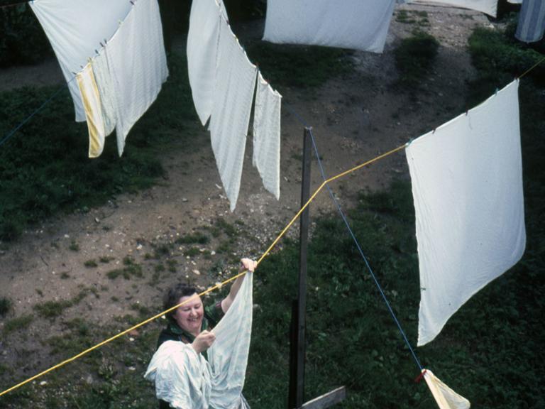 1960er Jahre: Eine Frau hängt Wäsche an einer Wäscheleine draußen auf.