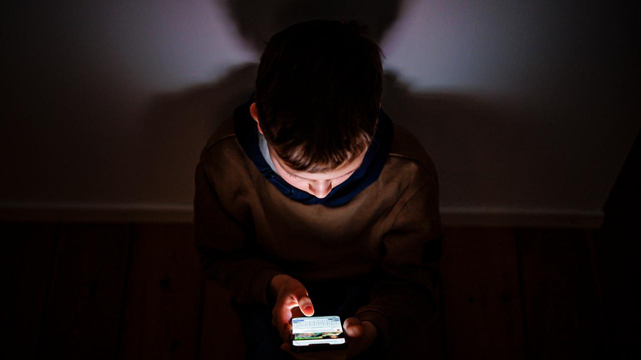 Symbolfoto zum Thema Kinder nutzen Social Media: Ein Junge sitzt in einem dunklen Raum, sein Gesicht wird von einem Smartphone beleuchtet.