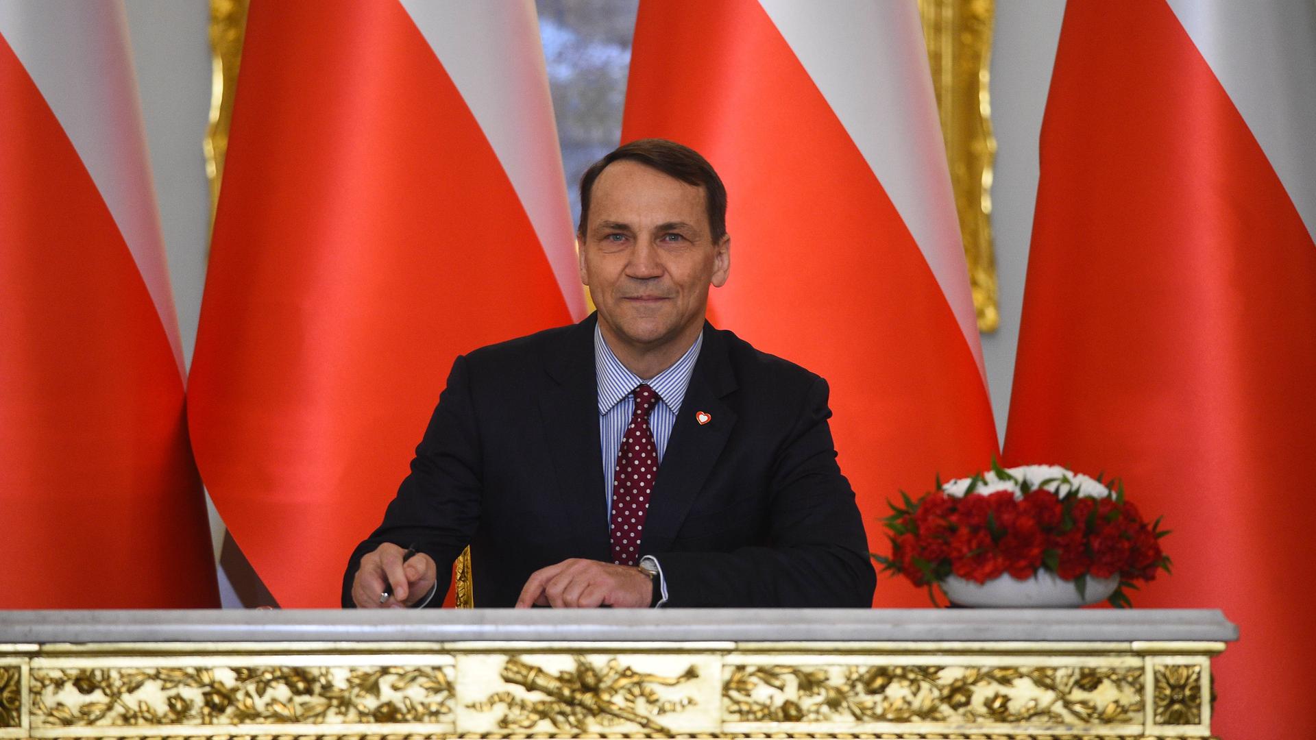 Der polnische Innenminister Sikorski sitzt an einem Tisch vor polnischen Flaggen.