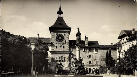 Ein historisches Schwarz-Weiß-Foto aus den 1930er-Jahren zeigt das Stadtzentrum von Murten mit Uhrturm, Denkmal und Laternen.
