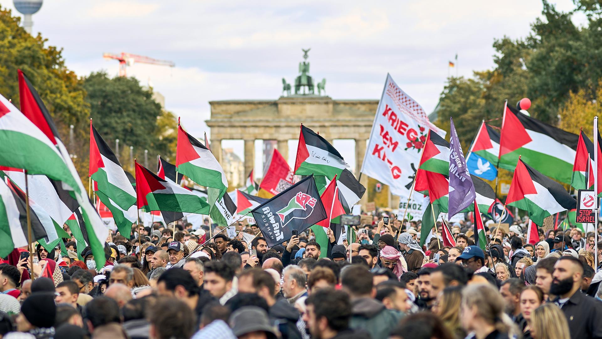 Demonstranten schwenken palästinensische Fahnen und halten Plakate hoch. Im Hintergrund ist das Brandenburger Tor zu sehen