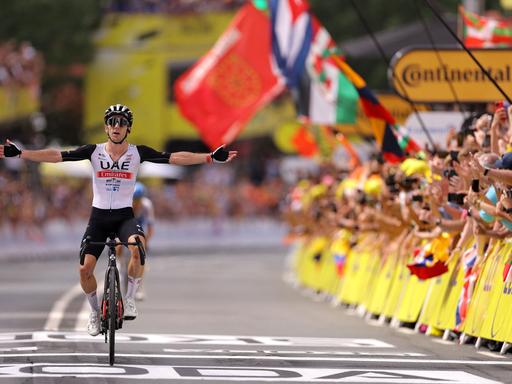 Bei der ersten Zieleinfahrt der Tour de France 2023 hebt der britische Fahrer Adam Yates feiernd die Arme. 