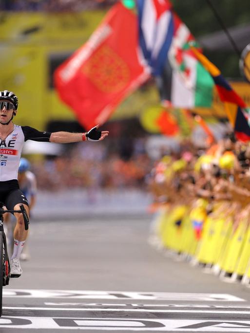Bei der ersten Zieleinfahrt der Tour de France 2023 hebt der britische Fahrer Adam Yates feiernd die Arme. 