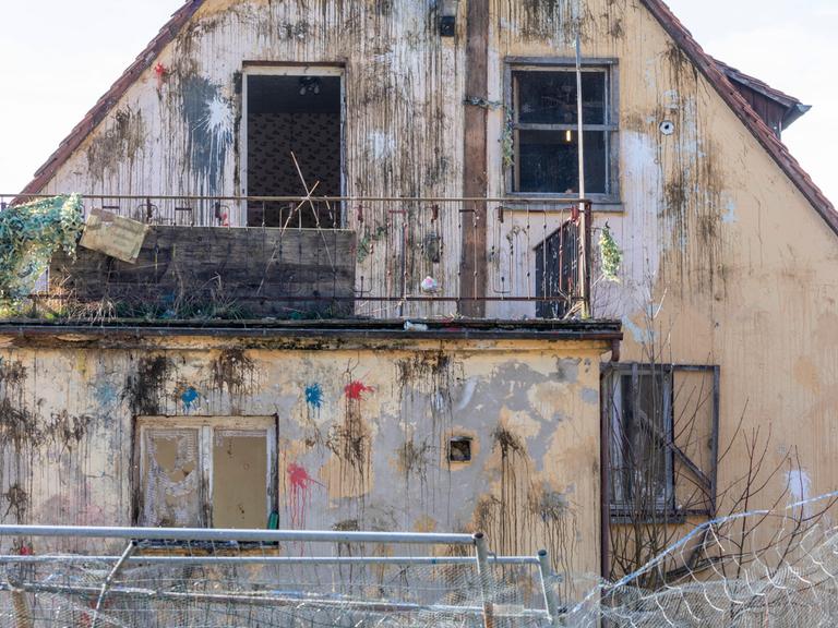 Frontalansicht der Fassade eines Hauses im desolaten Zustan, das mit zahlreichen Farbbeutel beworfen wurde.