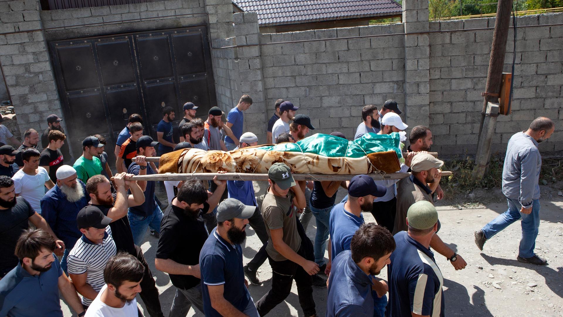 Beerdigung von dem Opfer des Tiergartenmörders, Selimchan Changoschwili, im August 2019 in Georgien. Zahlreiche Männer tragen den in eine Decke eingewickelten Leichnam.  