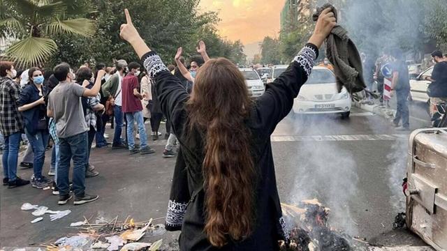 Eine Frau steht bei Protesten in der iranischen Hauptstadt Teheran ohne das vorgeschrieben Kopftuch auf einer Staße und streckt die Arme in die Luft