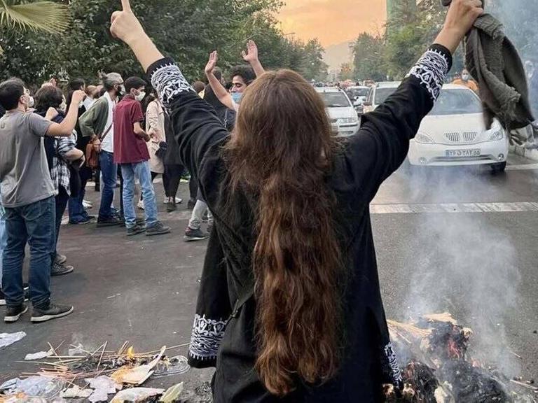 Eine Frau steht bei Protesten in der iranischen Hauptstadt Teheran ohne das vorgeschrieben Kopftuch auf einer Staße und streckt die Arme in die Luft