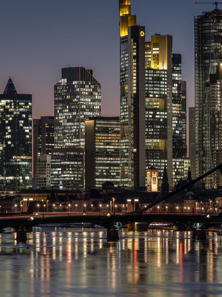 Die Hochhäuser der Frankfurter Skyline am Abend mit dem Main als Vordergrund.