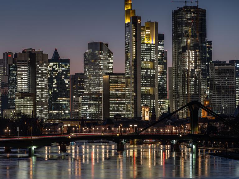 Die Hochhäuser der Frankfurter Skyline am Abend mit dem Main als Vordergrund.