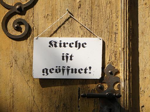 "Kirche ist geöffnet" steht auf dem Schild an einer Kirchentür