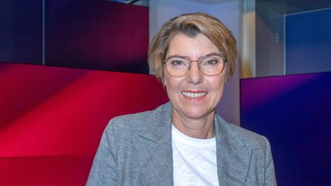 Bettina Böttinger mit wei2em T-Shirt und grauer Jacke im Studio bei Maischberger. Sie guckt in die Kamera.