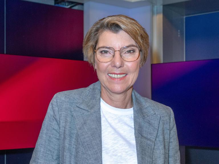 Bettina Böttinger mit wei2em T-Shirt und grauer Jacke im Studio bei Maischberger. Sie guckt in die Kamera.