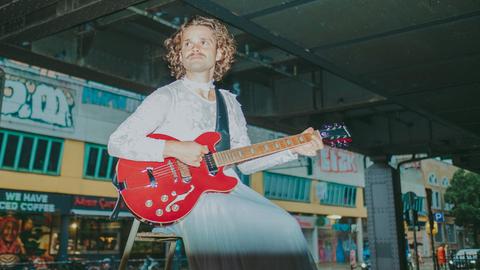 Tristan Brusch sitzt unter einer Berliner U-Bahn-Trasse und spielt eine knallrote E-Gitarre.
