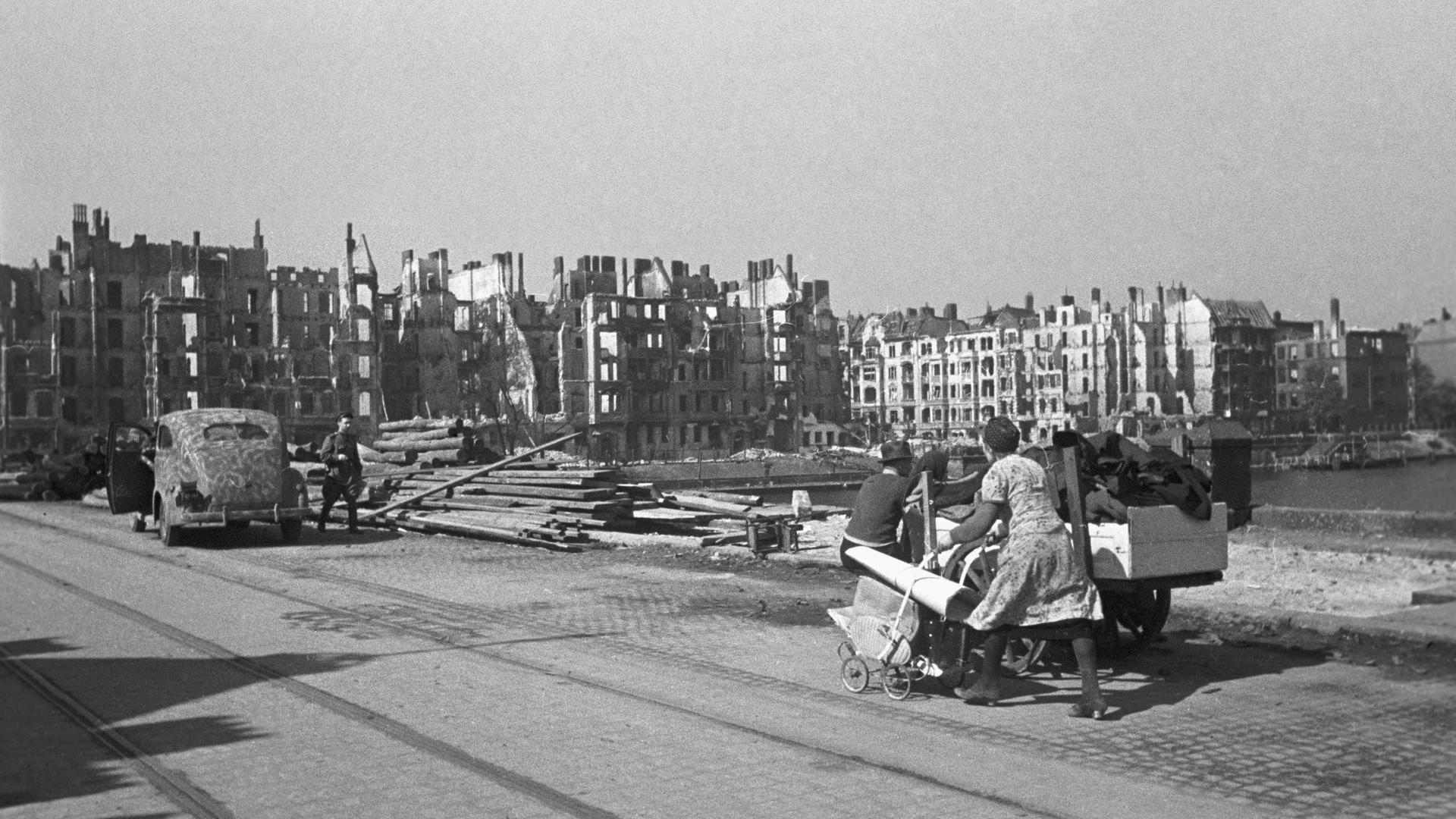 Am Spreeufer in Berlin bei Kriegsende 1945: Eine Frau schiebt einen Kinderwagen voll Gegenstände vor einer Reihe komplett zerstörter Häuser durch die Stadt.