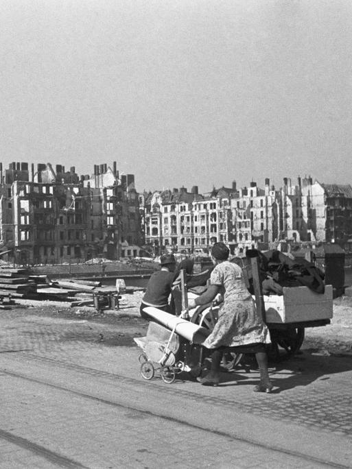 Am Spreeufer in Berlin bei Kriegsende 1945: Eine Frau schiebt einen Kinderwagen voll Gegenstände vor einer Reihe komplett zerstörter Häuser durch die Stadt.