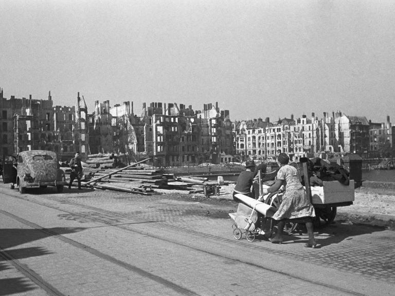 Am Spreeufer in Berlin bei Kriegsende 1945: Eine Frau schiebt einen Kinderwagen voll Gegenstände vor einer Reihe komplett zerstörter Häuser durch die Stadt.